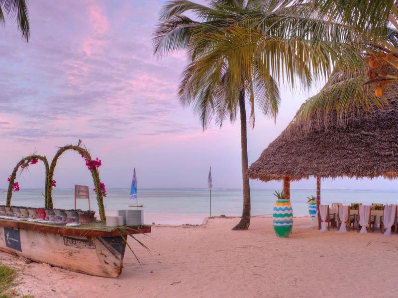 Strandrestaurant mit Palmen, Tischen und Stühlen bei Sonnenuntergang am Meer