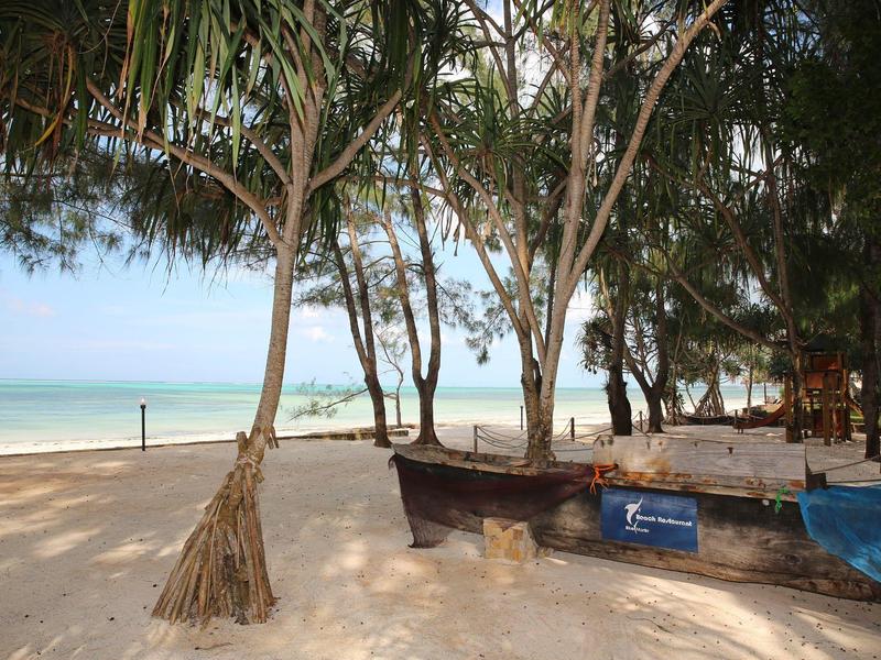 Strand mit Bäumen, Booten und ruhigem Meer im Hintergrund an einem sonnigen Tag.