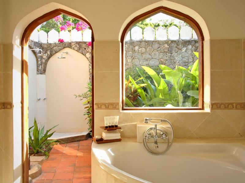 Helles Badezimmer mit runder Badewanne, Bogenfenster und Blick auf einen Garten mit Pflanzen.