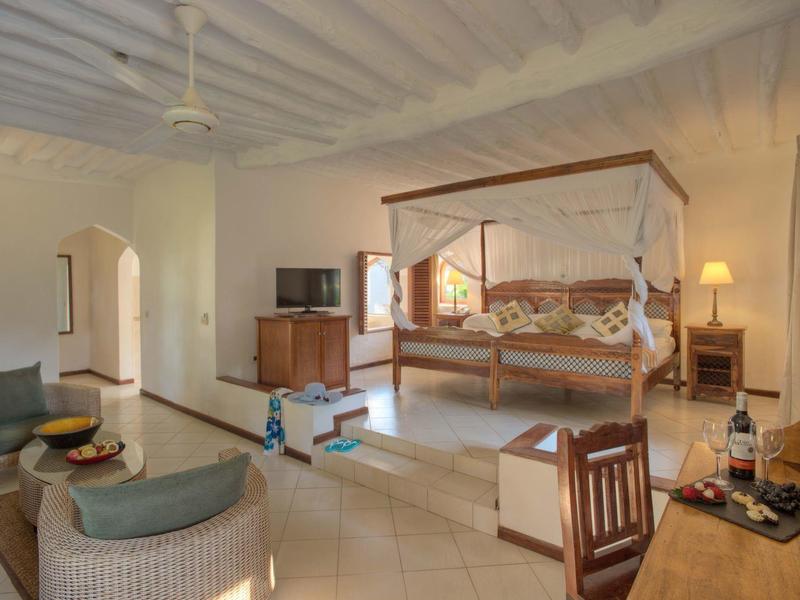 Helles Hotelzimmer mit Himmelbett, Sitzbereich und warmem Holzmobiliar.