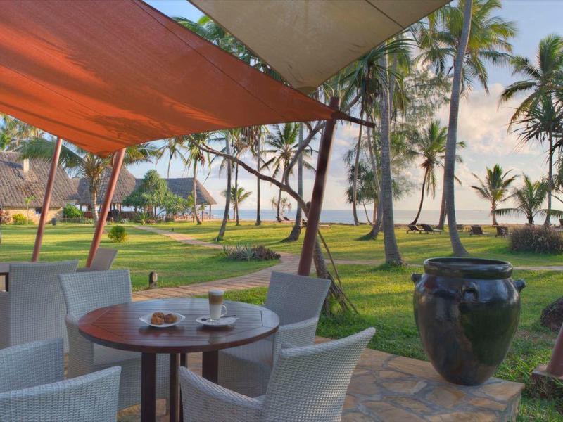 Terrasse mit weißen Stühlen und Tischen, Palmen und Blick auf den Strand bei Sonnenuntergang