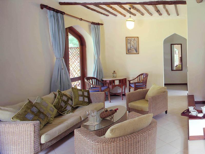 Helles Wohnzimmer mit Sofa, Sesseln, Holzbalkendecke und großem Fenster mit blauen Vorhängen.