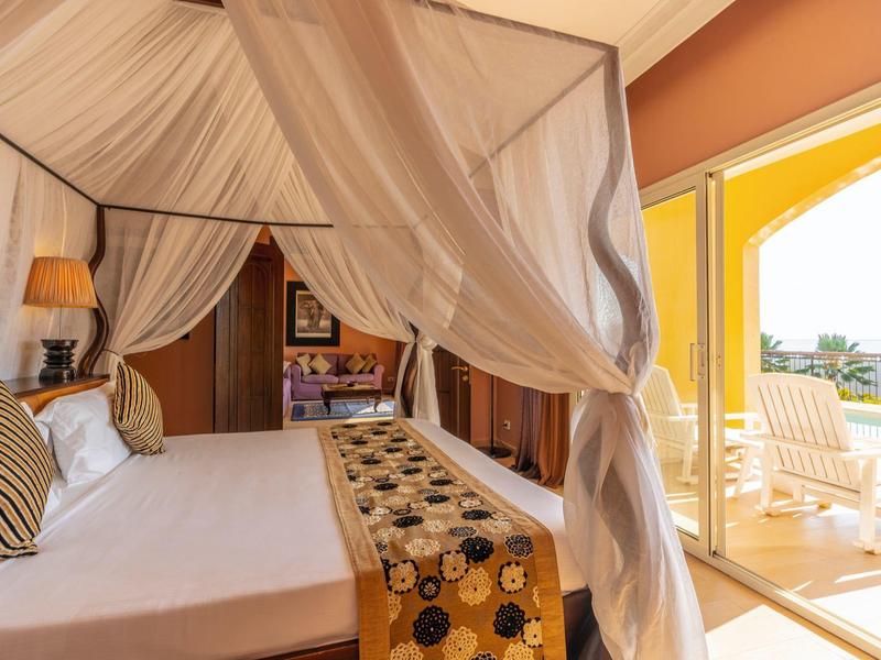 Hell eingerichtetes Schlafzimmer mit Moskitonetz, Doppelbett, Balkon und Meerblick.