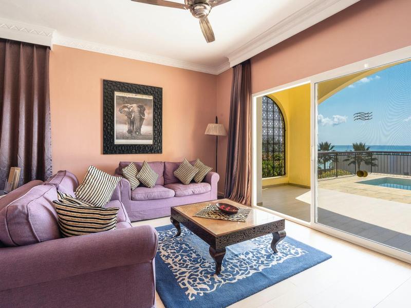 Helles Wohnzimmer mit lila Sofas, Teppich, dunklen Vorhängen und Meerblick durch große Schiebetür.