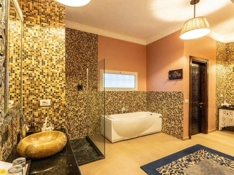 Luxuriöses Badezimmer mit goldenen Mosaikfliesen, freistehender Badewanne und modernen Armaturen.