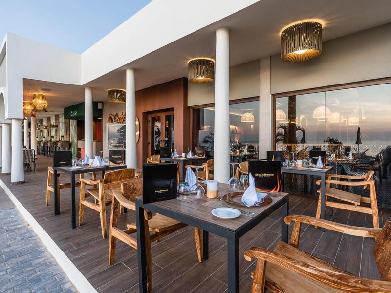 Restaurantterrasse mit Holzmöbeln, gedeckten Tischen und modernen Laternen an weißen Säulen.
