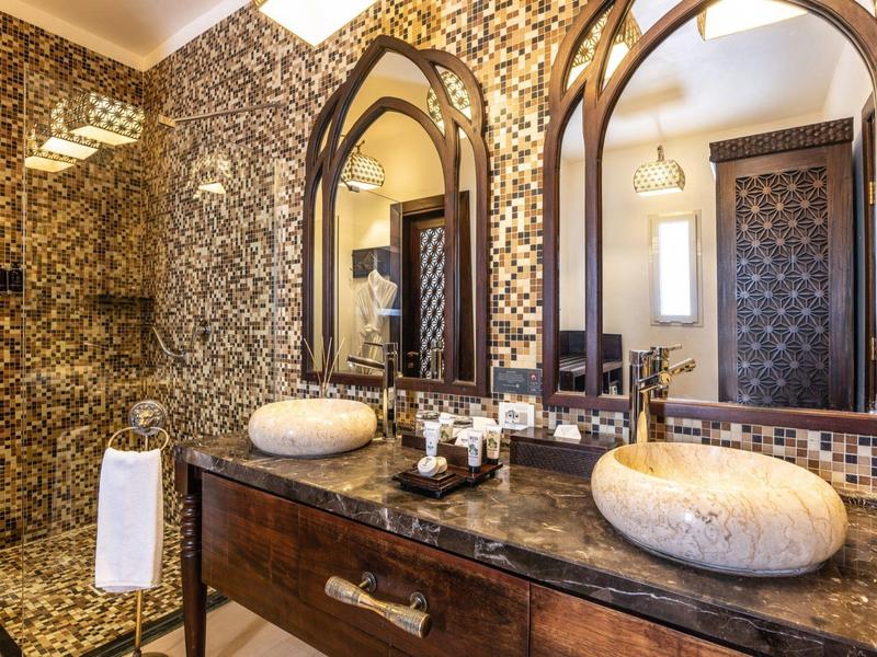 Elegantes Badezimmer mit Marmorwaschbecken, Spiegeln im Bogenstil und kunstvoller Wandgestaltung.