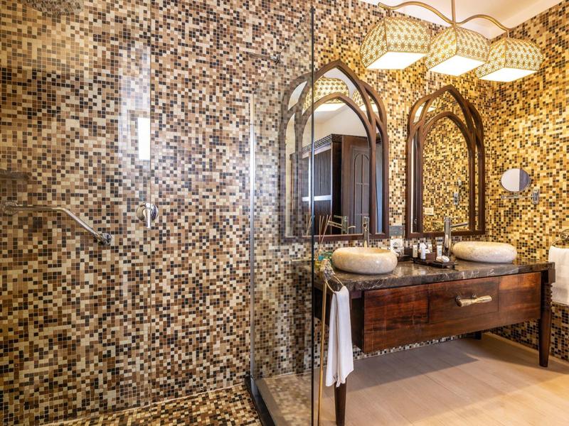 Modernes Badezimmer mit Mosaikdusche, dunklem Holzwaschtisch und zwei ovalen Spiegeln.