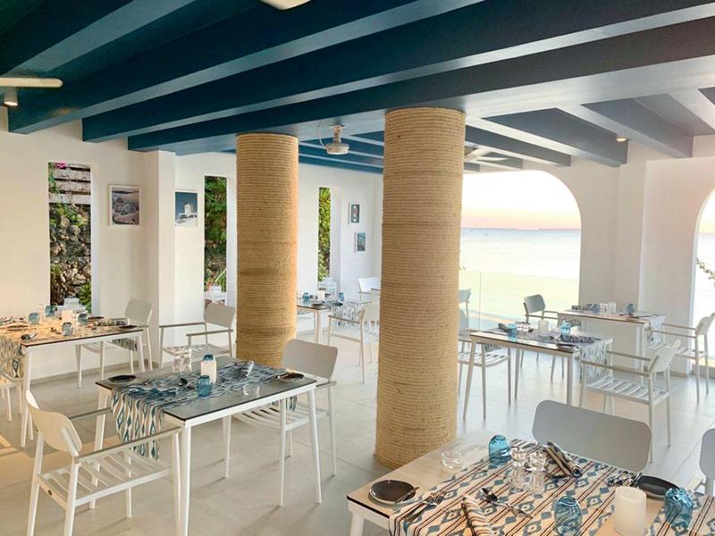 Moderner Restaurantbereich mit weißen Möbeln und Meerblick bei Sonnenuntergang.