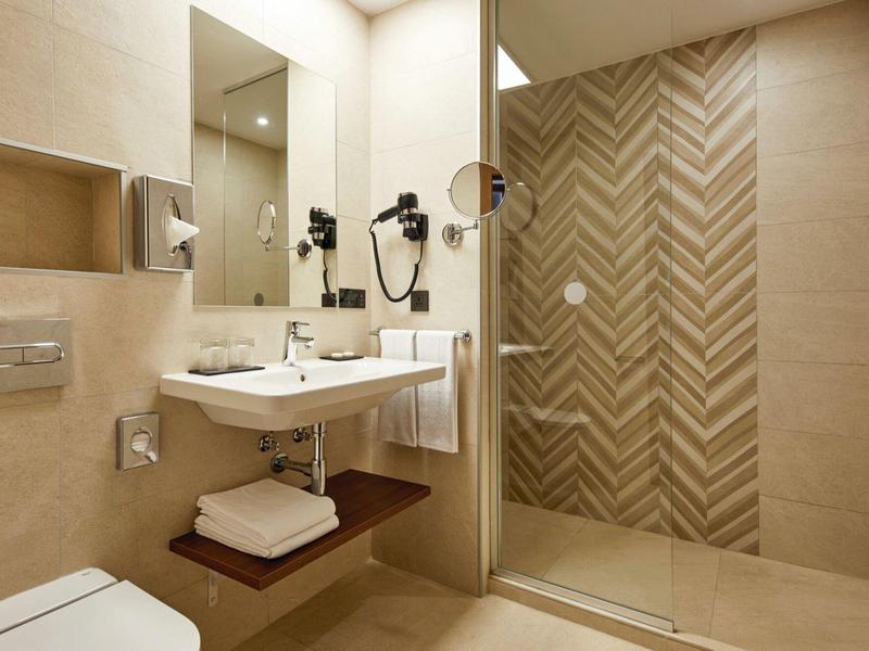 Modernes Badezimmer mit heller Fliesenwand, Glas-Duschabtrennung und hängendem Waschbecken.