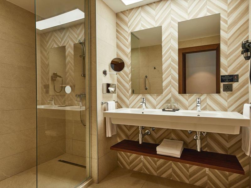 Modernes Badezimmer mit Doppelwaschtisch, großen Spiegeln, braunen Fliesen und einer Glasdusche.