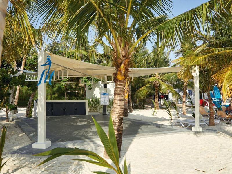 Strandbereich mit Sand, Palmen und einer Pergola mit Sonnenschutz.