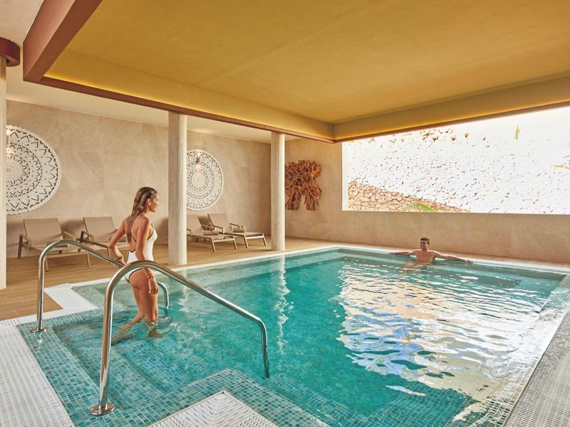 Innenpool mit hellen Wänden, großen Fenstern und Menschen beim Schwimmen und Entspannen.