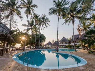Runder Swimmingpool umgeben von hohen Palmen und Bungalows bei Sonnenuntergang.