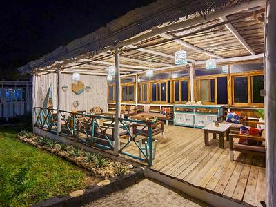 Überdachte Holzterrasse mit Sitzmöglichkeiten und Beleuchtung, umgeben von Gras und Zaun bei Nacht.