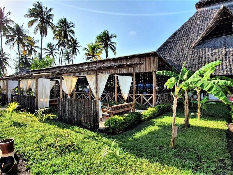 Tropisches Resort mit strohgedeckten Bungalows, Palmen und grünem Rasen unter klarem Himmel.