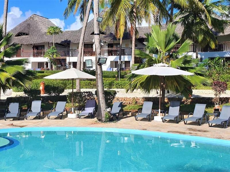 Großer blauer Pool vor Reihen von Liegestühlen, Palmen und mehrstöckigen Gebäuden im Hintergrund.