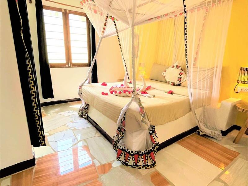 Hell eingerichtetes Schlafzimmer mit Bett, Moskitonetz und bunten Dekorationen, Fenster mit Vorhängen.