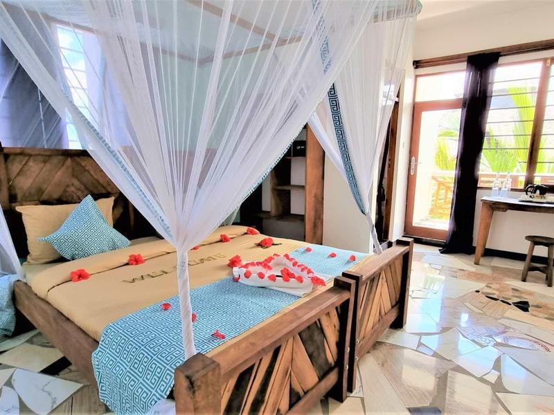 Helles Schlafzimmer mit Holzbetten, weißen Moskitonetzen, blauen Akzenten und Fliesenboden.