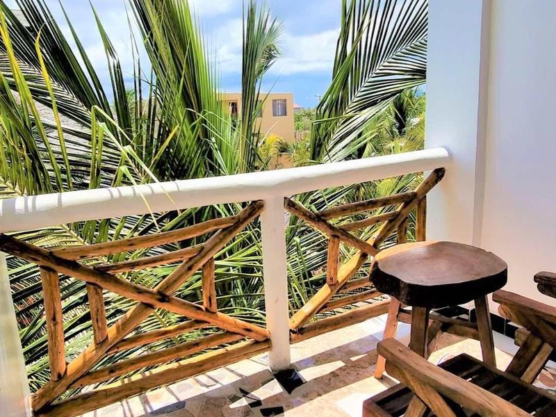 Balkon mit Holzmöbeln, Blick auf Palmen und blauem Himmel mit Wolken.