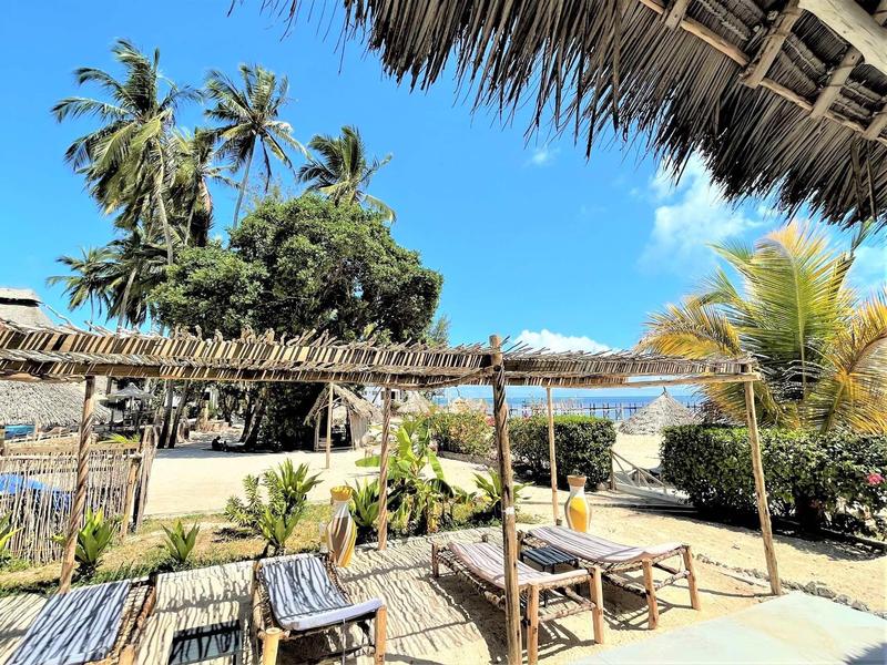 Strandrestaurant mit Holztischen, Stühlen, Palmen und klarem blauem Himmel im Hintergrund.