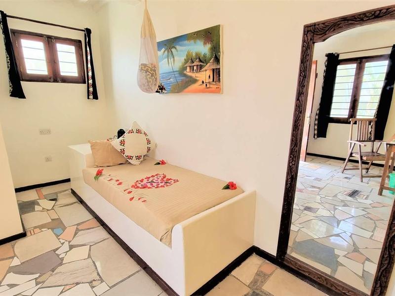 Helles Zimmer mit Einzelbett, Holzrahmen-Spiegel, Fenster mit Holzläden und Mosaikboden.