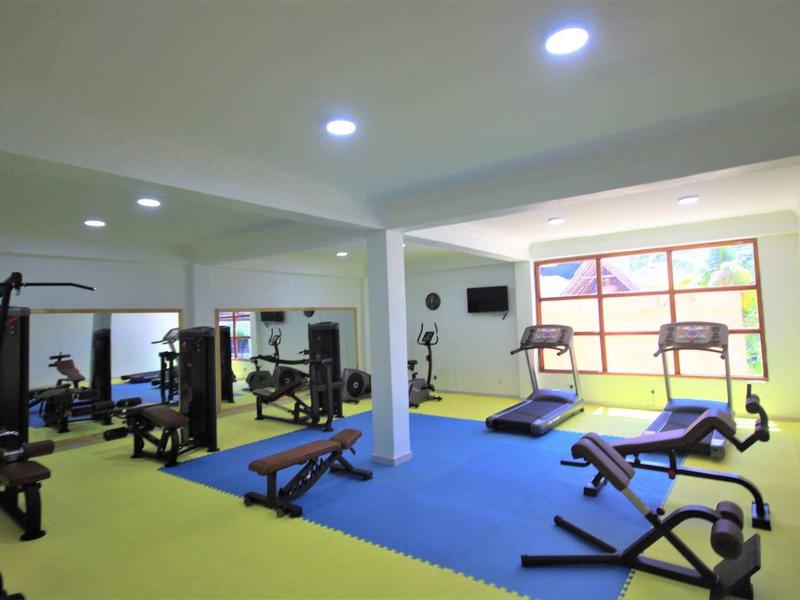 Heller Fitnessraum mit grünen und blauen Bodenmatten, Trainingsgeräten und großen Fenstern.