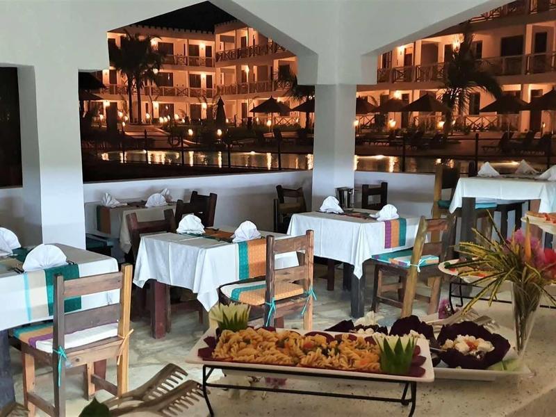 Restaurant mit gedeckten Tischen, Holzstühlen und Buffet mit verschiedenen Speisen an der Wand.