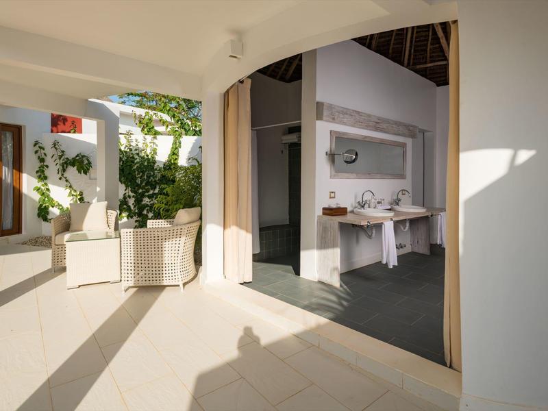 Helle Terrasse mit heller Bodenfliese, weißen Wänden, Pflanzen und offenem Blick ins moderne Wohnzimmer.