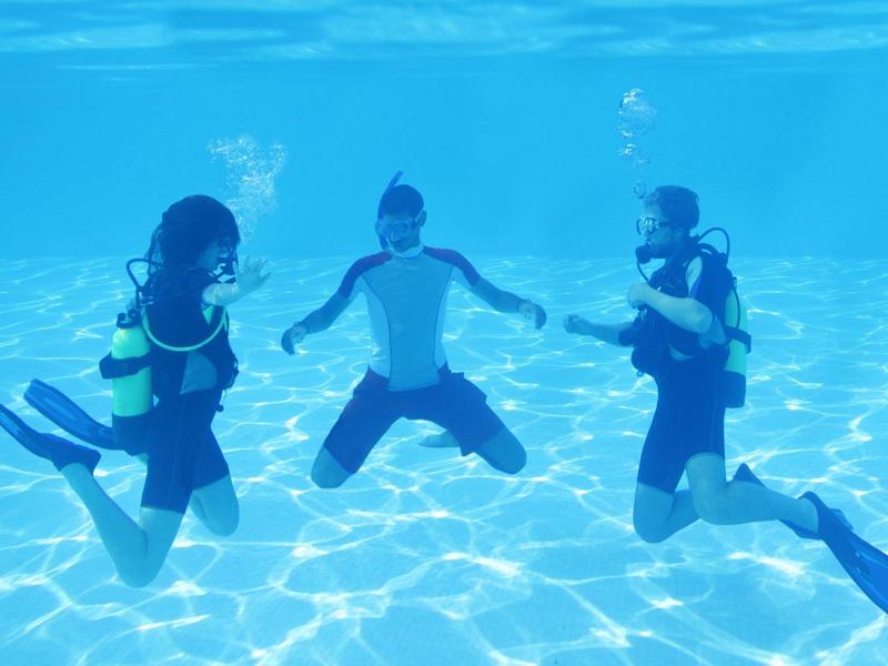 Drei taucher unterwasser mit ausrüstung, blaues licht und klare wassertiefe sichtbar.