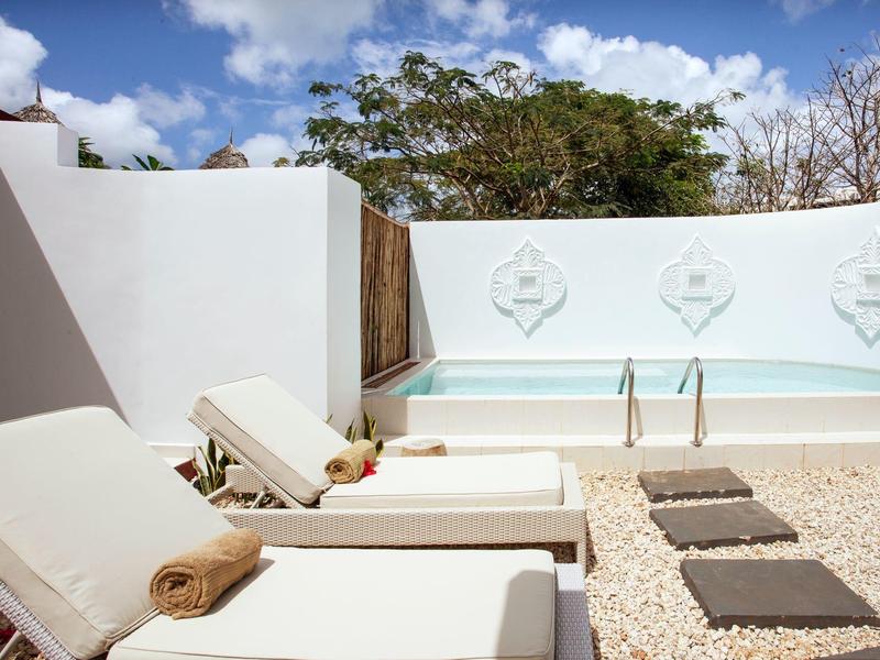 Drei weiße Liegestühle an Pool mit heller Steinfläche und blauen Himmel mit Wolken.