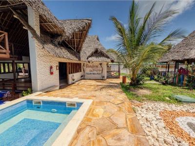 Außenbereich mit kleinem blauen Pool, Natursteinboden, Palmen und strohgedeckten Bungalows.