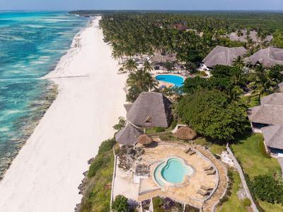 Weißer Sandstrand, türkisfarbenes Meer, grüne Palmen und runde Pools neben Bungalows mit Strohdächern.
