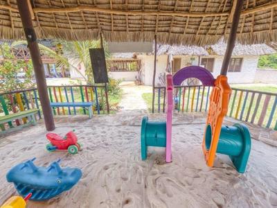 Überdachter Kinderspielplatz mit Sandboden, Rutsche, Klettergerüst und bunten Spielgeräten.