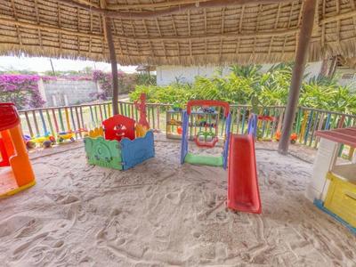 Überdachter Sandspielplatz mit Rutsche, Spielhäusern und verschiedenen bunten Spielgeräten.