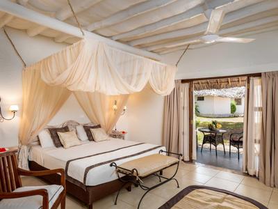 Helles Schlafzimmer mit Himmelbett, beiger Moskitonetz, Holzmöbeln und Zugang zur Terrasse.