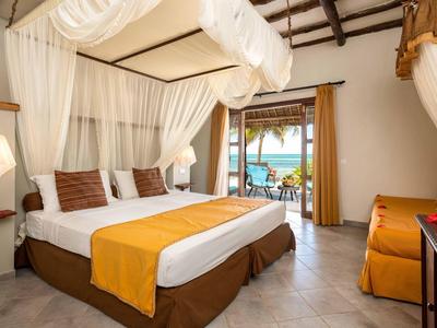 Helles Schlafzimmer mit Himmelbett, braunen Kissen, orangenem Bettläufer und Balkon mit Meerblick.