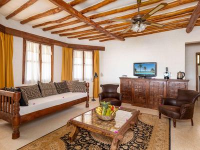 Wohnzimmer mit Holzdecke, braunen Möbeln, gelben Vorhängen und einem Fernseher auf Sideboard.