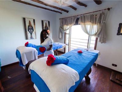 Gemütlicher Behandlungsraum mit zwei blauen Massageliegen, Fenster und dekorativer Holzmöbel.