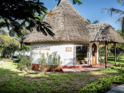 Ein rundes Haus mit Strohdach, weiß getünchte Wände, umgeben von grünem Gras und Palmen.