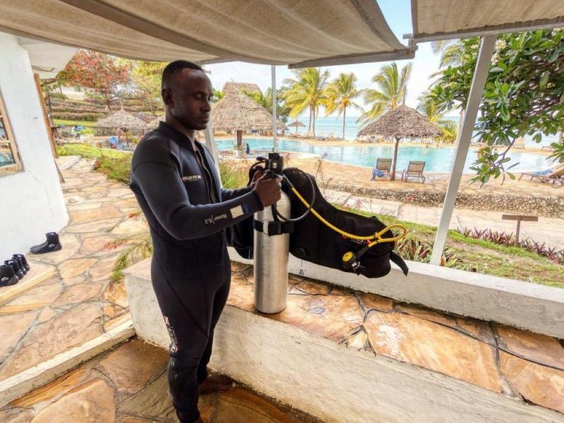 Persoon in duikuitrusting bereidt zich voor bij een buitenwasbak met landschap op de achtergrond.
