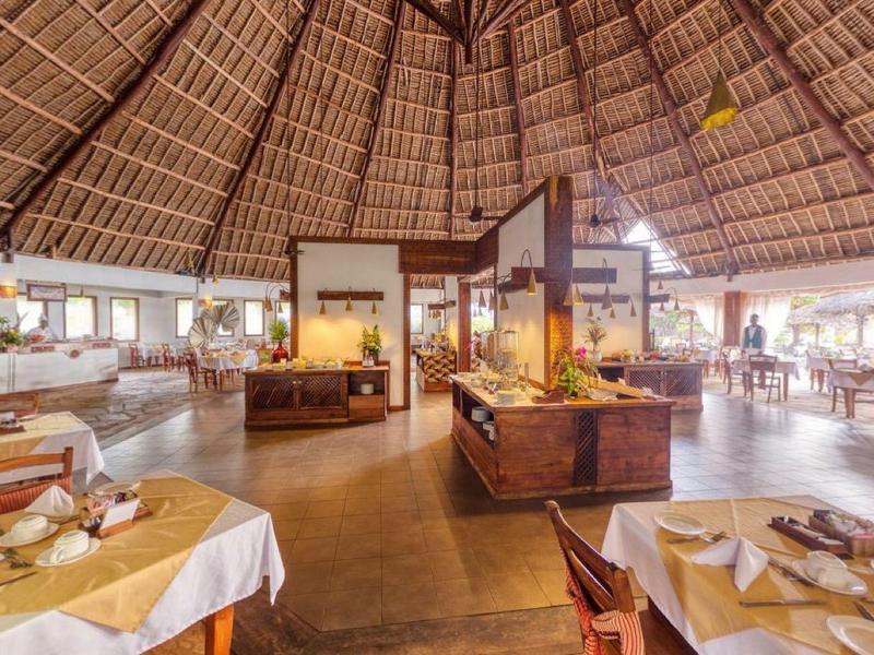 Ruim restaurant met hoog rieten dak, houten meubels en elegant gedekte tafels.