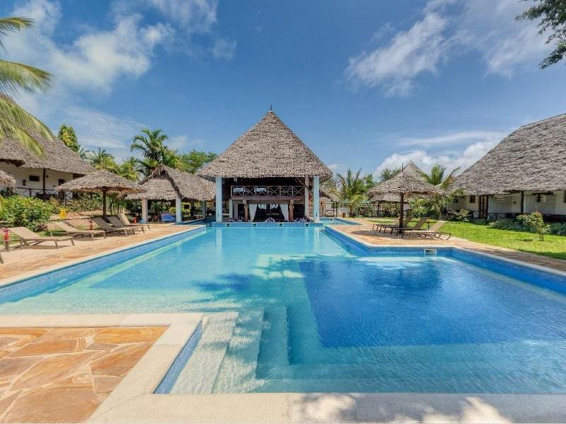 Groot zwembad met palmbomen en rieten hutten onder een blauwe hemel bij een resort.