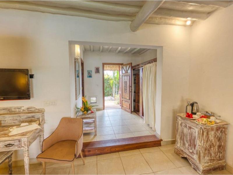 Gezellige kamer met houten plafond, stoel, tv en open uitzicht op een tuin.