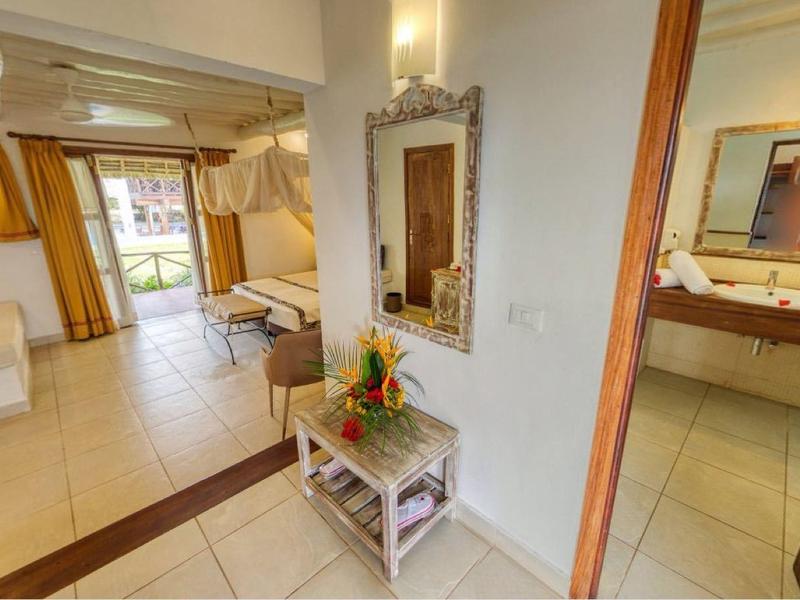 Lichte hotelkamer met bed, bank, betegelde vloer en aangrenzende badkamer.