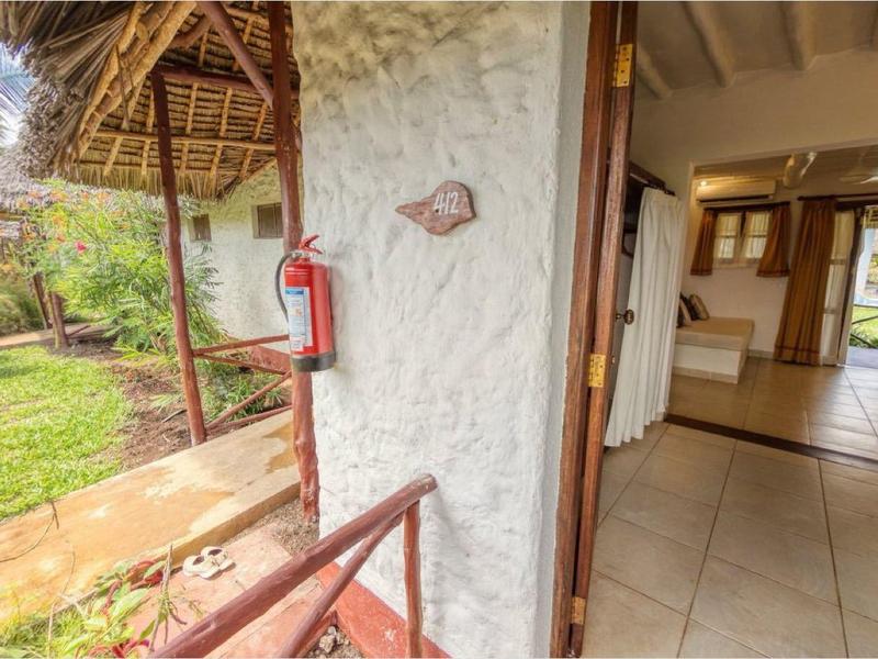 Open ingang naar een lichte kamer met uitzicht op een tuin en palmbomen.