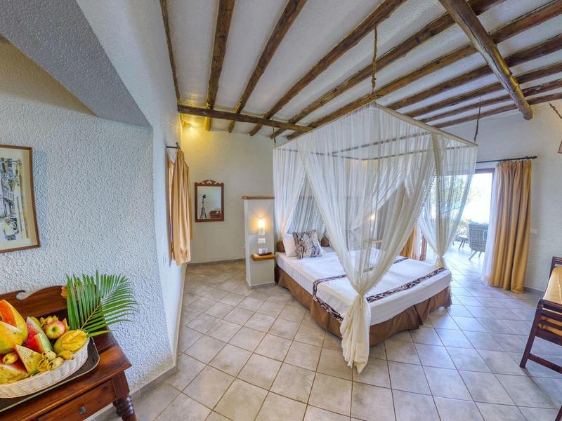 Licht ingericht hotelkamer met hemelbed, fruitschaal en houten meubels.