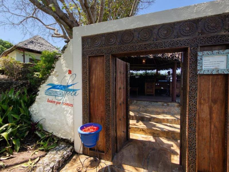 Houten deur in oude witte muur met planten en huizen op de achtergrond.