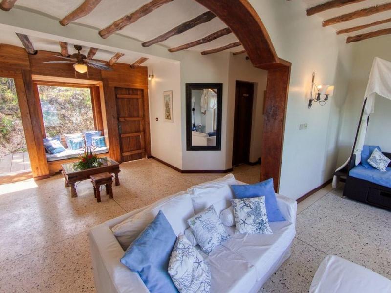 Licht hotelkamer met blauwe bank, hemelbed en grote ramen met uitzicht op stenen tuin.