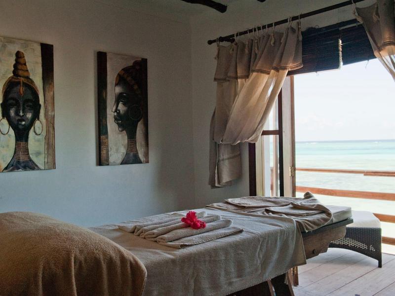 Massagetafel met handdoeken en zeezicht door open deur in lichte kamer.